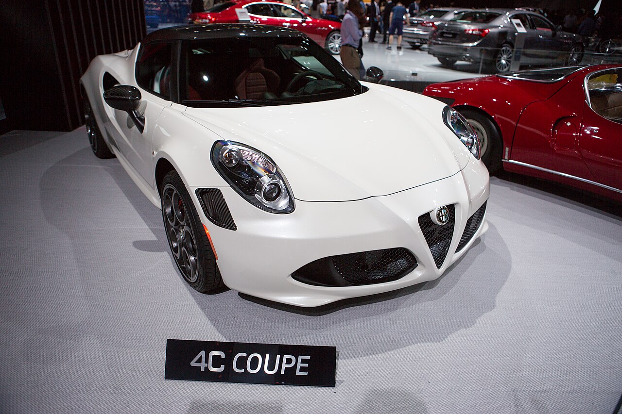 White Alfa Romeo 4C Coupe with a black roof on a show stand, front right three-quarter view at the 2015 Los Angeles Auto Show.