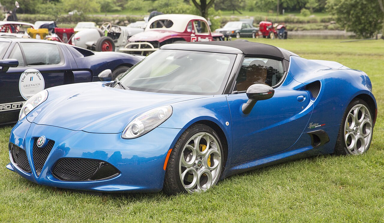 Blue 2020 Alfa Romeo 4C Spider with its black roof in place, front left three-quarter view on grass at a concours.