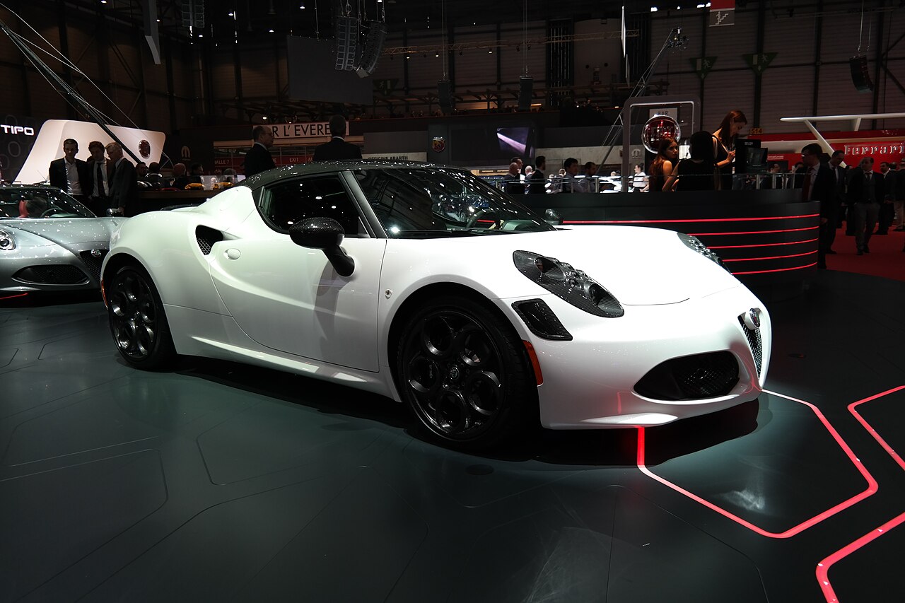 White Alfa Romeo 4C coupe with black wheels and a dark roof on a show stand, front right three-quarter view at the Geneva Motor Show.