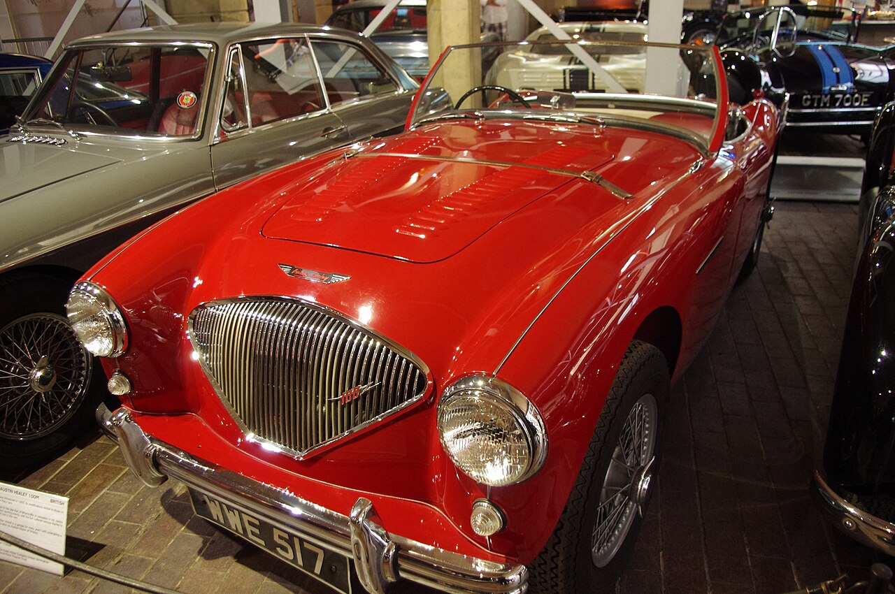 Red 1956 Austin-Healey 100M with a louvred bonnet and wire wheels, front left three-quarter view in a museum.