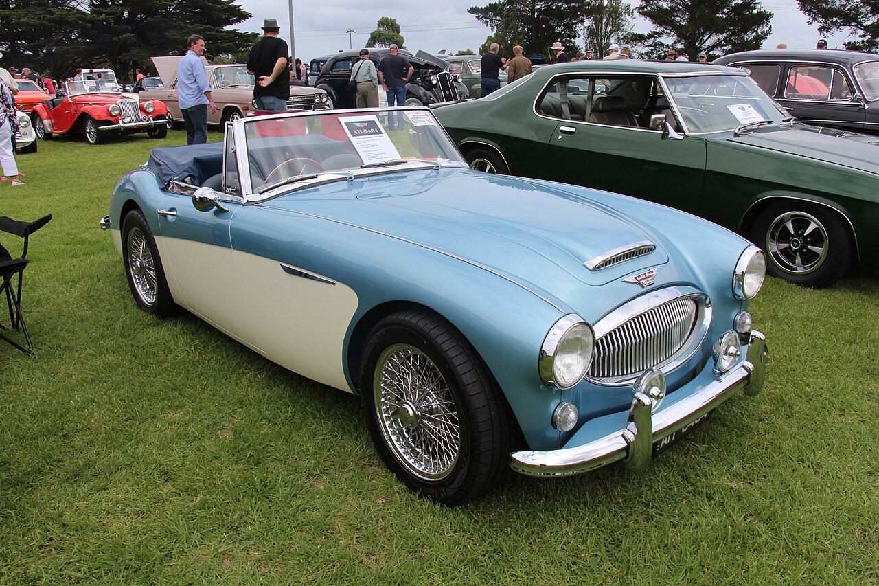 Pale blue and cream 1965 Austin-Healey 3000 Mk III with its roof down and wire wheels, front right three-quarter view on grass.