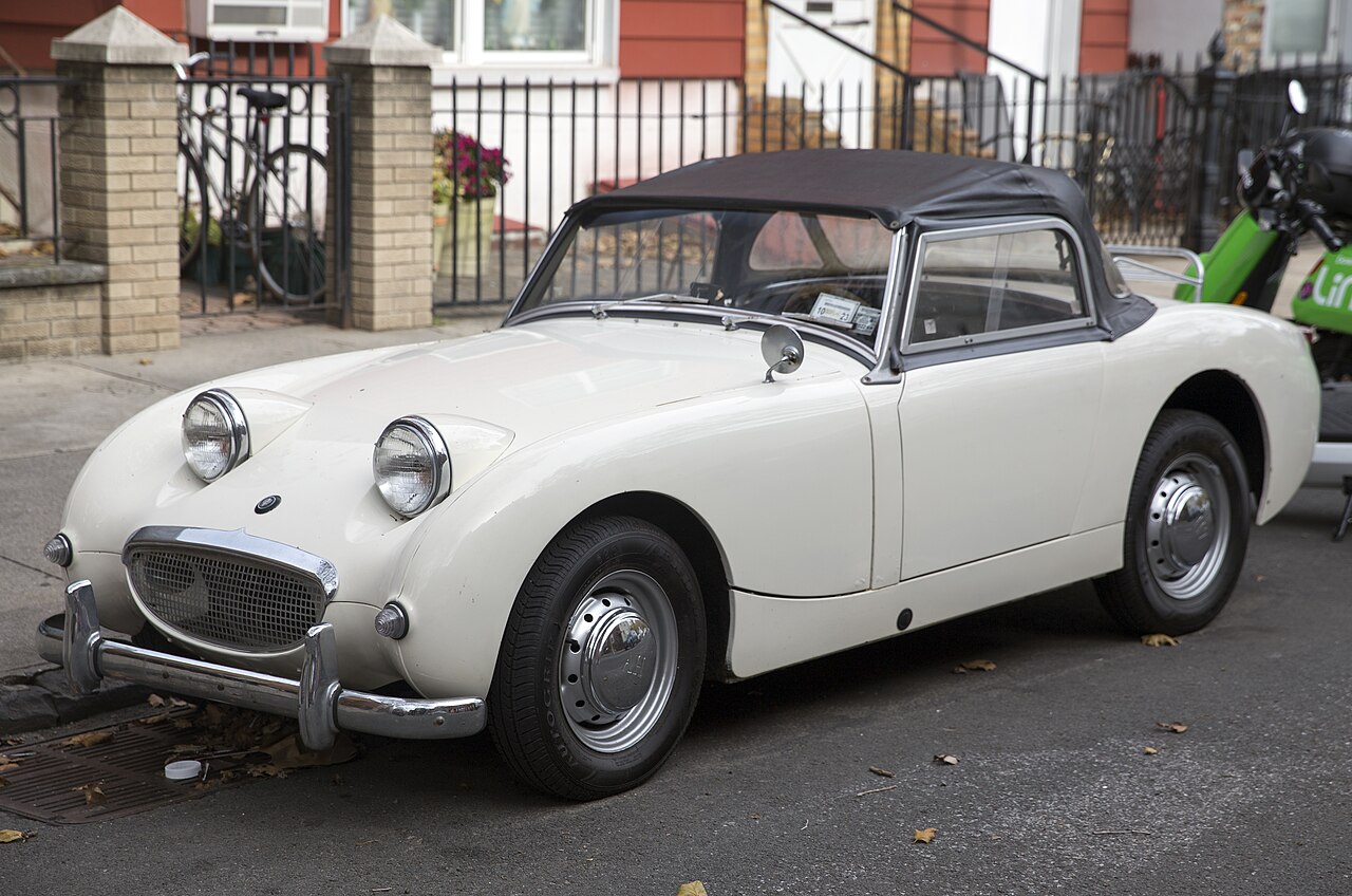 Cream 1960 Austin-Healey Sprite Mark I with its dark soft top up, front left three-quarter view parked on a city street.