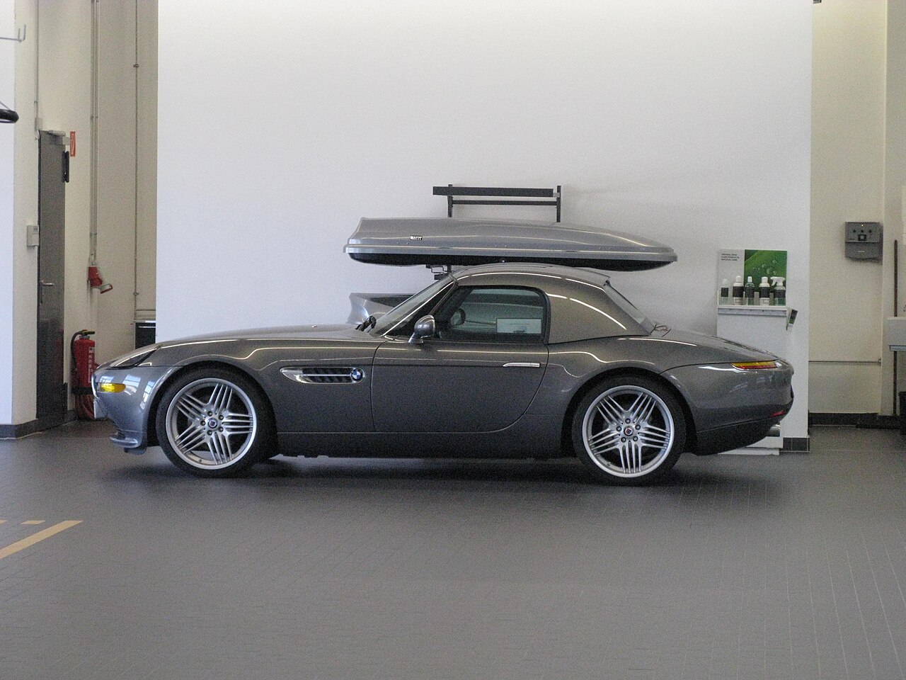 Grey BMW Alpina V8 Roadster with its hardtop fitted and Alpina wheels, side-on view indoors at a BMW dealership.