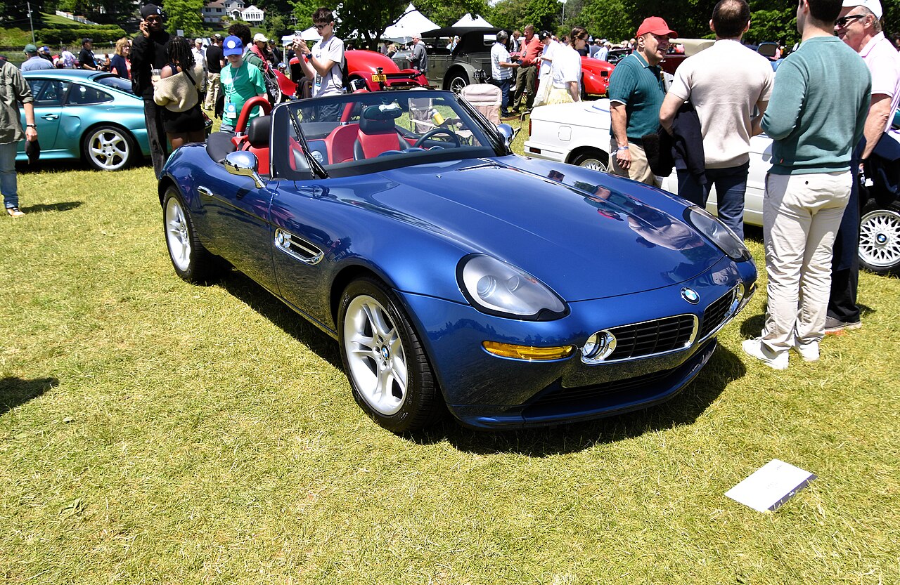 Blue 2002 BMW Z8 roadster with a red and black interior and its roof down, seen from the front right on a lawn at a car show.