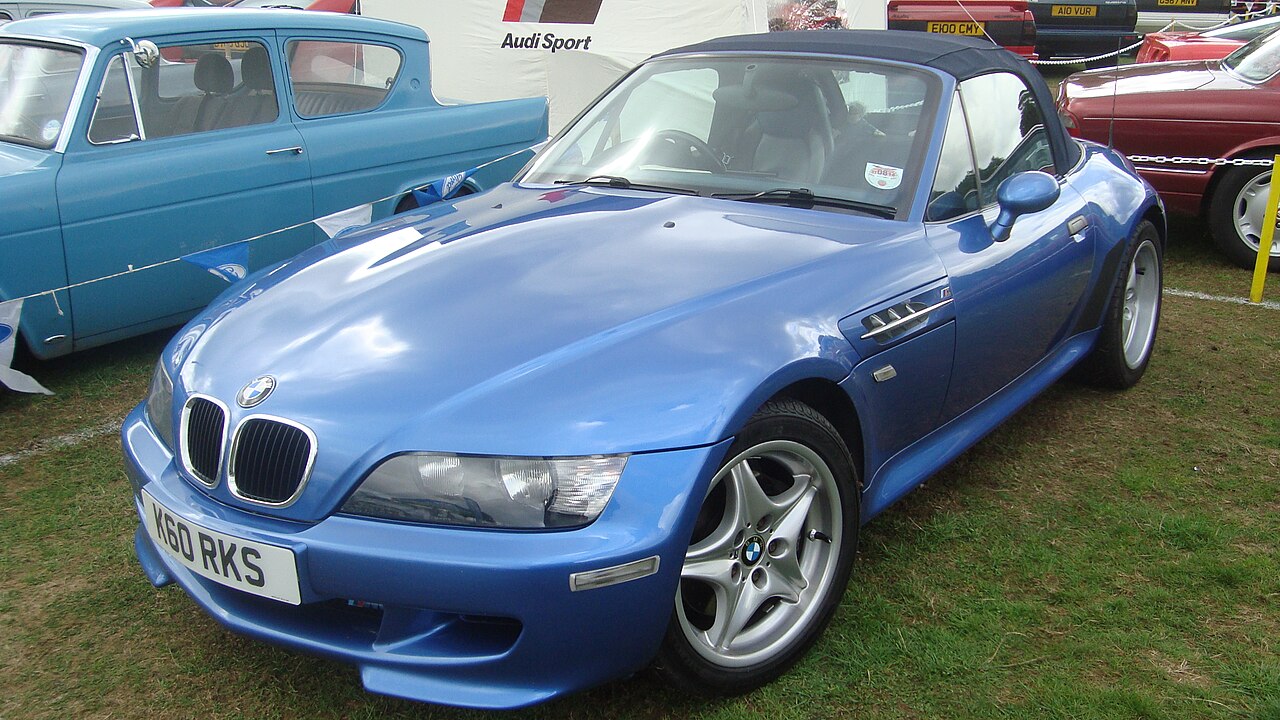 Blue 1999 BMW Z3 M Roadster with its soft top up, front three-quarter view on grass at a classic car show.