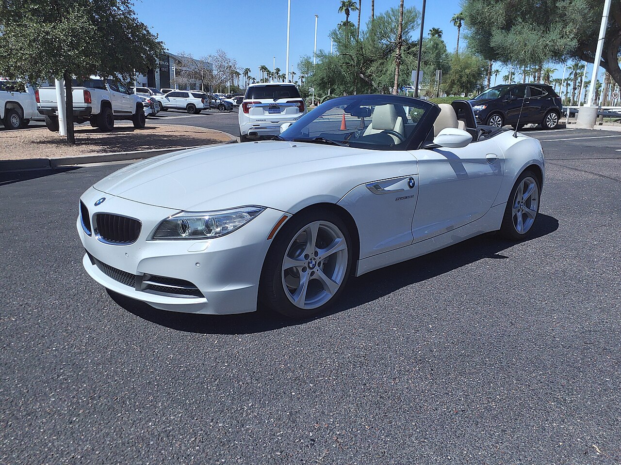 White BMW Z4 sDrive28i with its roof down, front left three-quarter view in a sunny car park.