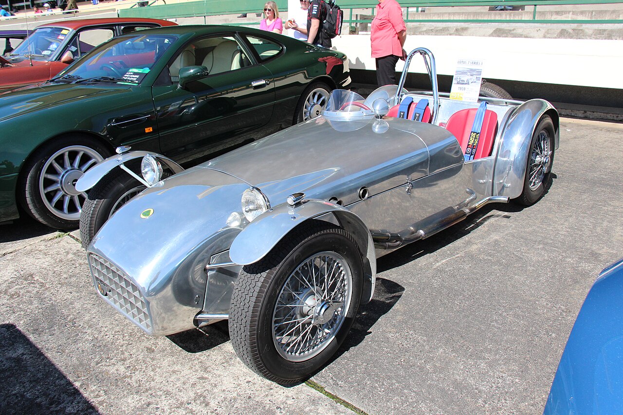 Polished aluminium Lotus Super Seven Series 1 with cycle wings, wire wheels and red seats, front left three-quarter view at a car show.