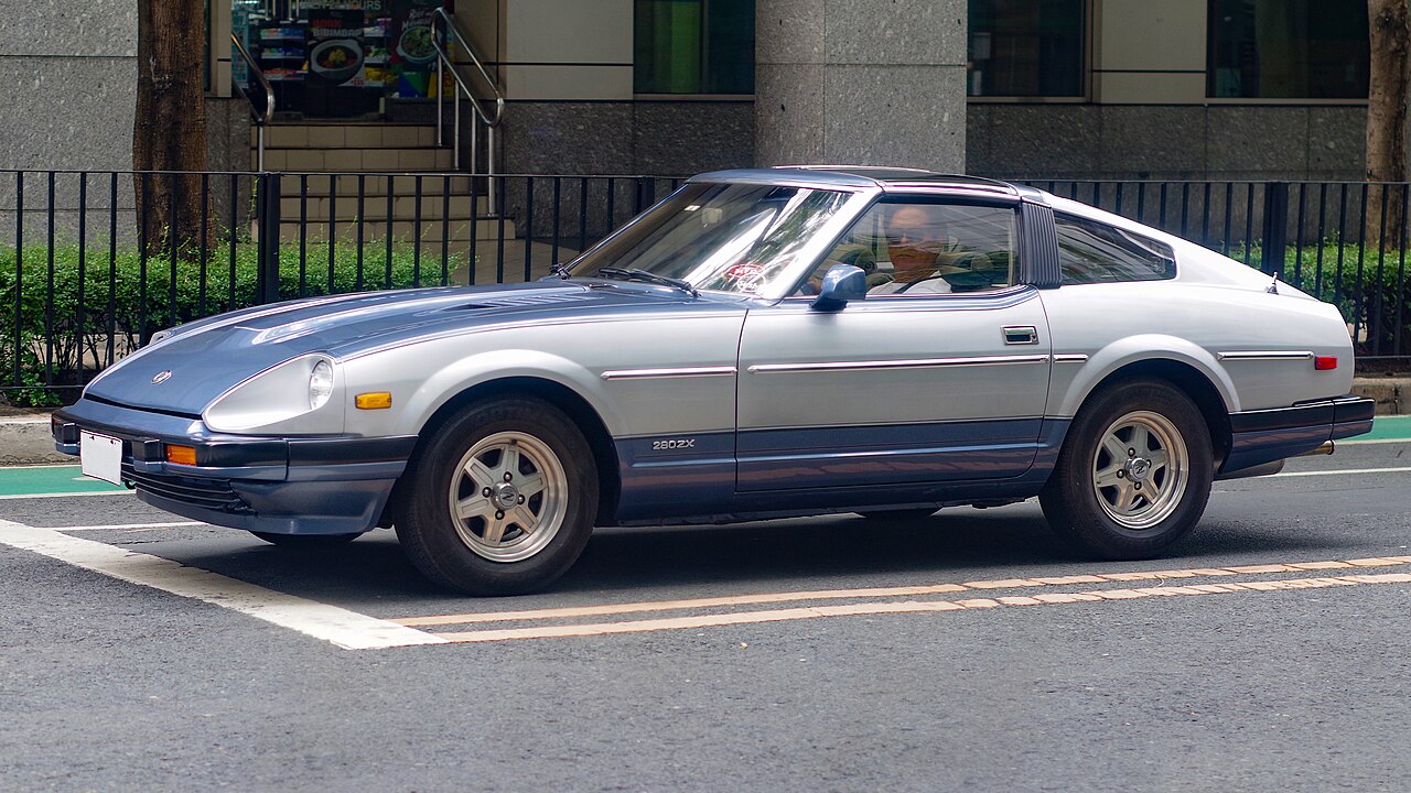 1983 Datsun 280ZX in two-tone silver and blue-grey, front left three-quarter view on a city street.