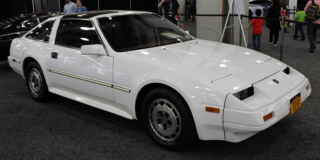 White 1986 Nissan 300ZX with a gold side stripe, front right three-quarter view on an auto show floor.