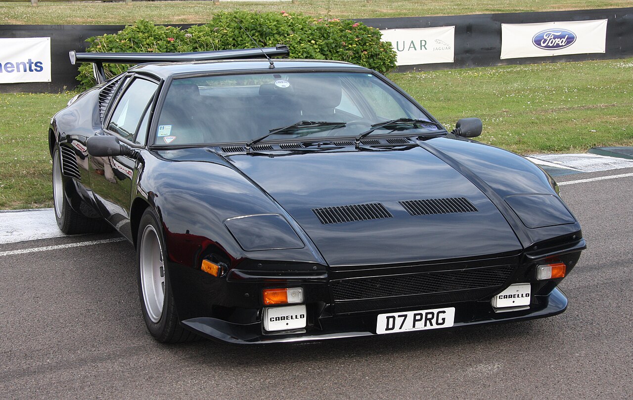 Black De Tomaso Pantera with wide flared arches and a large rear wing, front three-quarter view at a race circuit.