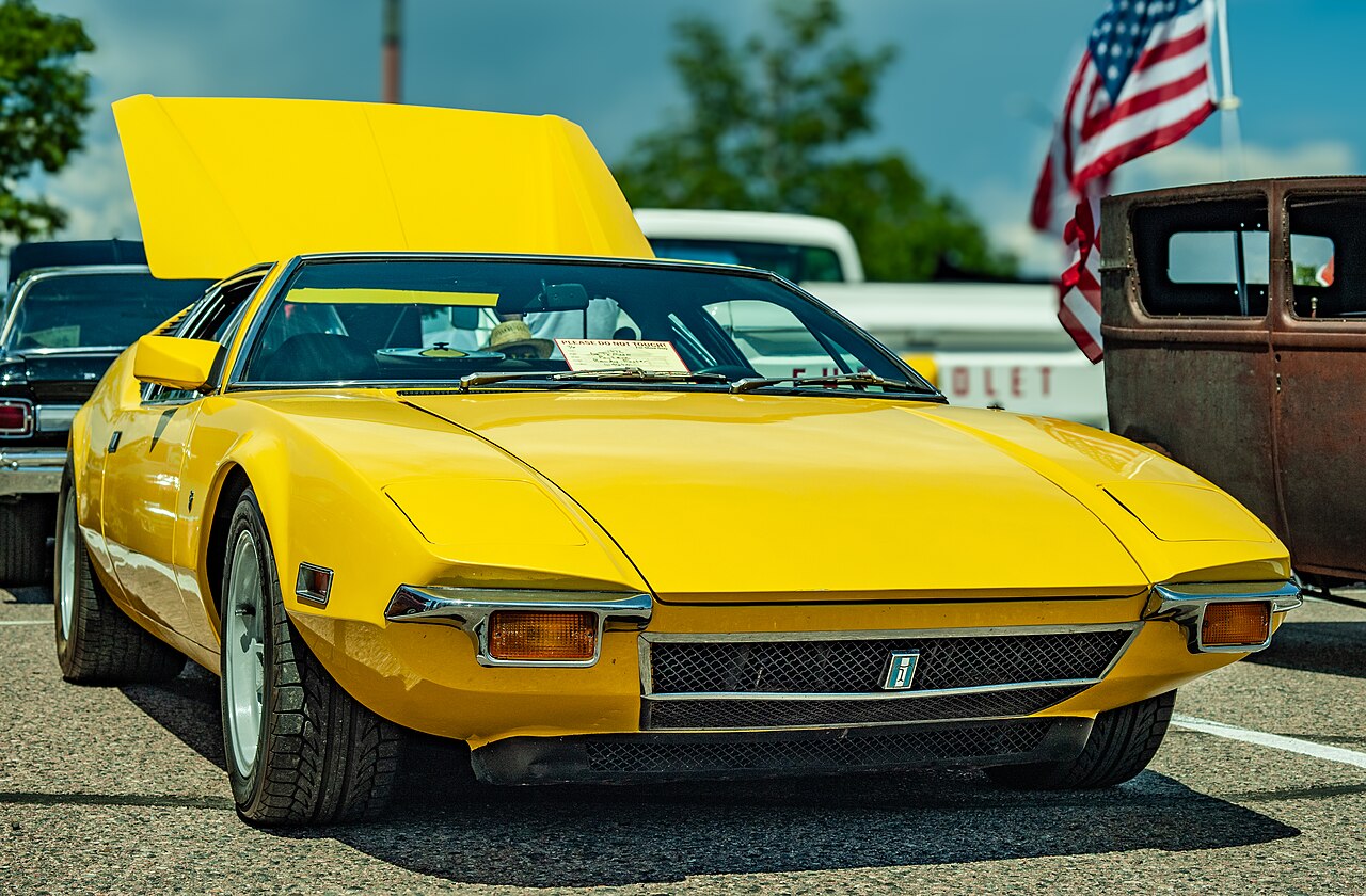Yellow 1972 De Tomaso Pantera seen almost head-on from the front right at a car show, with its engine lid raised.