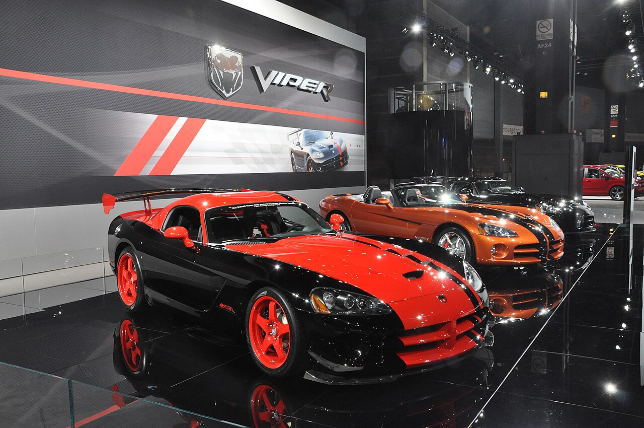 Black and red Dodge Viper coupe with red wheels and a big rear wing on a show stand, with an orange Viper roadster behind.