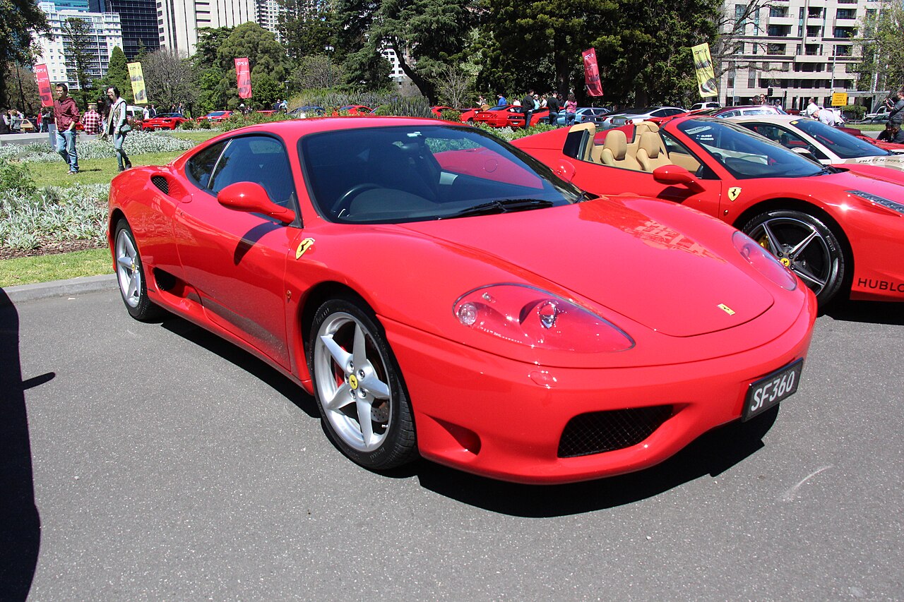 Red 2002 Ferrari 360 Modena coupe, front three-quarter view at an outdoor car event.