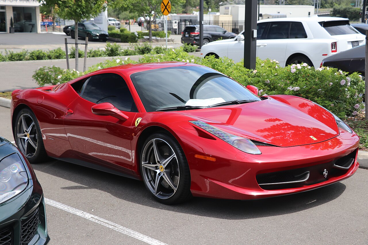 Red 2014 Ferrari 458 Italia, front right three-quarter view in a car park with a flowering hedge behind it.