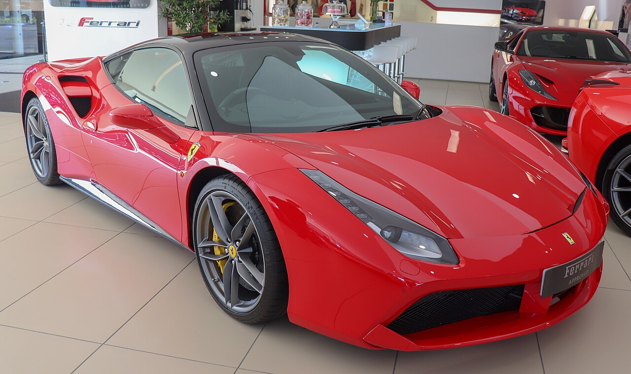 Red 2017 Ferrari 488 GTB with a black roof, front right three-quarter view in a showroom with other red Ferraris behind it.