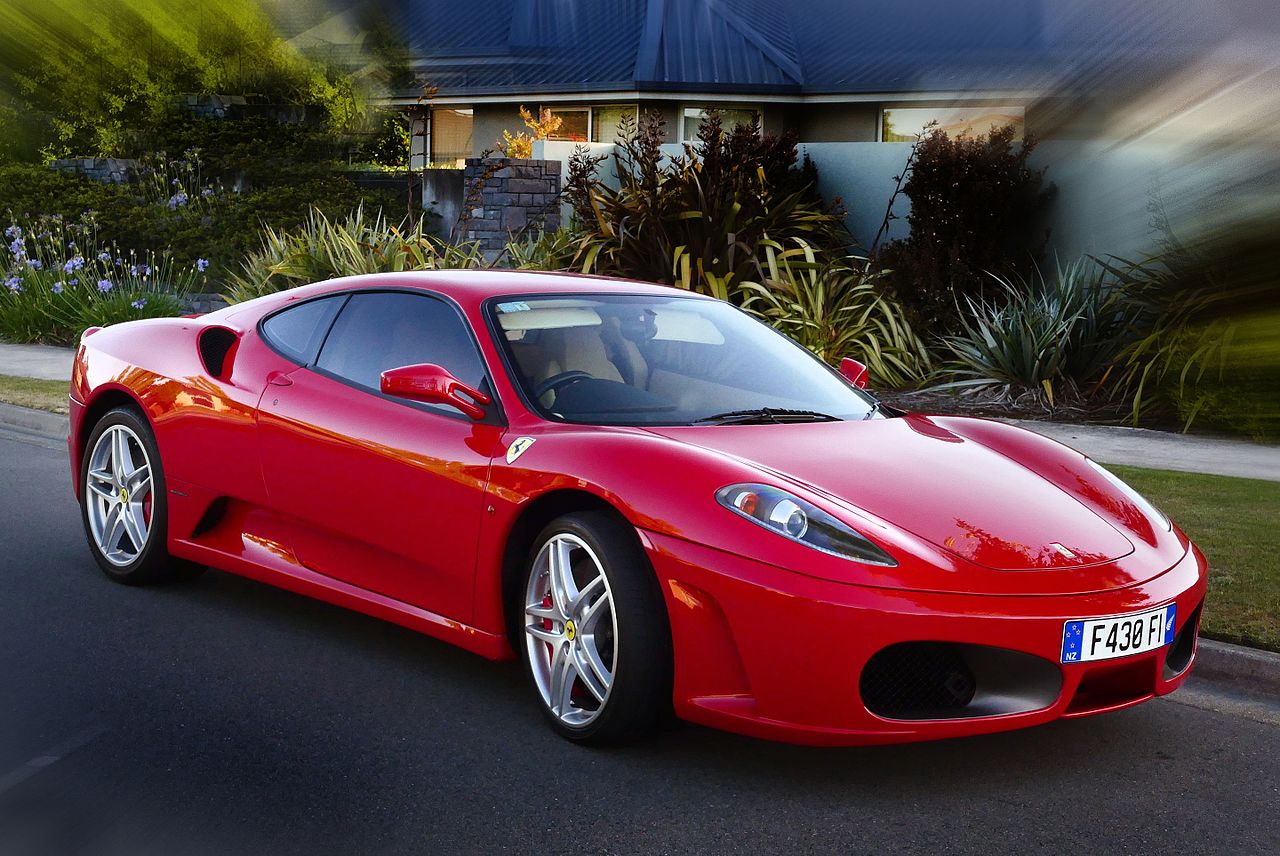 Red Ferrari F430 coupe with silver wheels, front three-quarter view beside a suburban kerb.