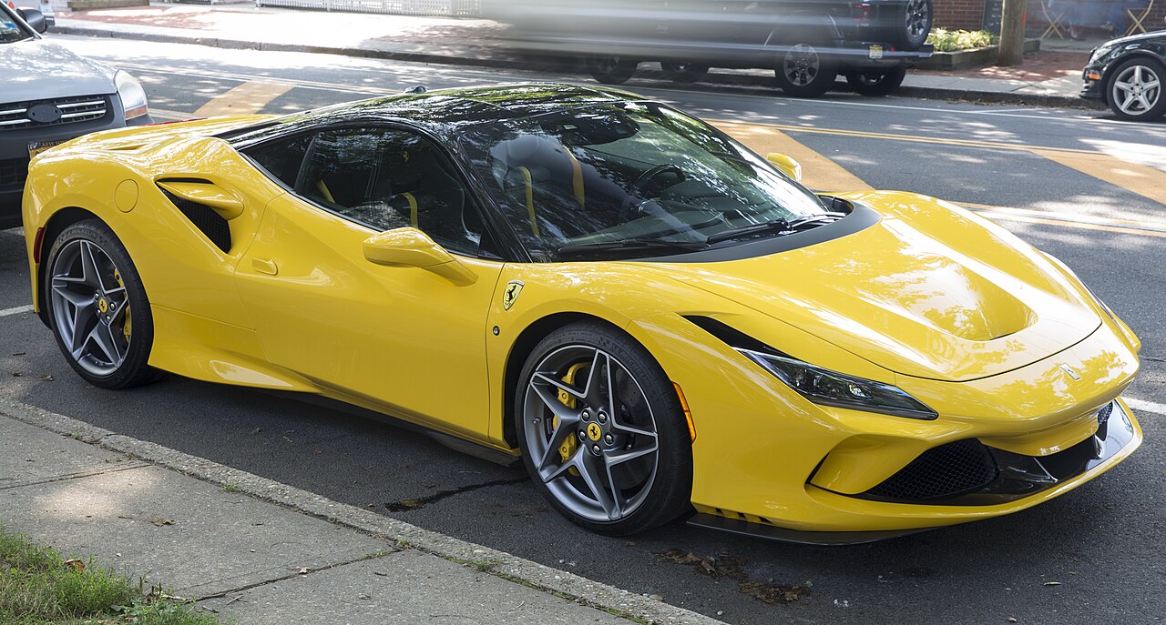 Yellow 2020 Ferrari F8 Tributo with a black roof, front right three-quarter view parked at the kerb on a street.