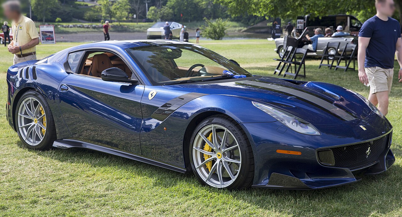 Blue 2017 Ferrari F12tdf with yellow brake calipers, front right three-quarter view on a lawn at a concours.