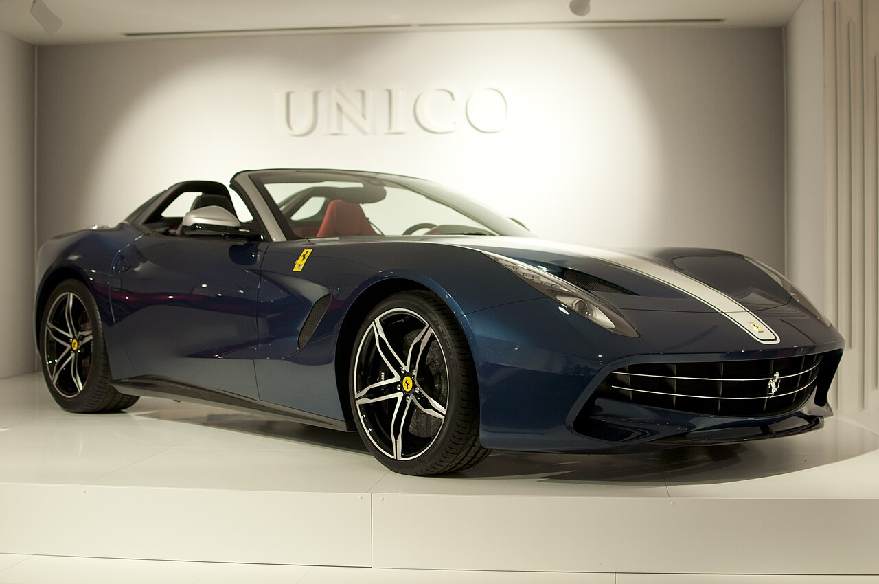 Dark blue open-top Ferrari F60 America with a silver bonnet stripe, front right three-quarter view on a white stand in the Ferrari museum.