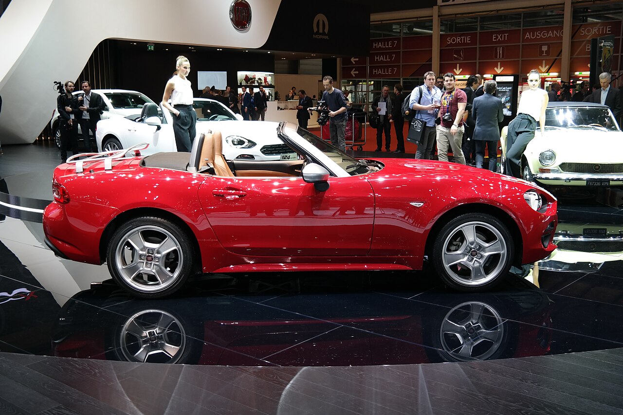 Red Fiat 124 Spider with its roof down, seen side-on on a display stand at the 2016 Geneva Motor Show.