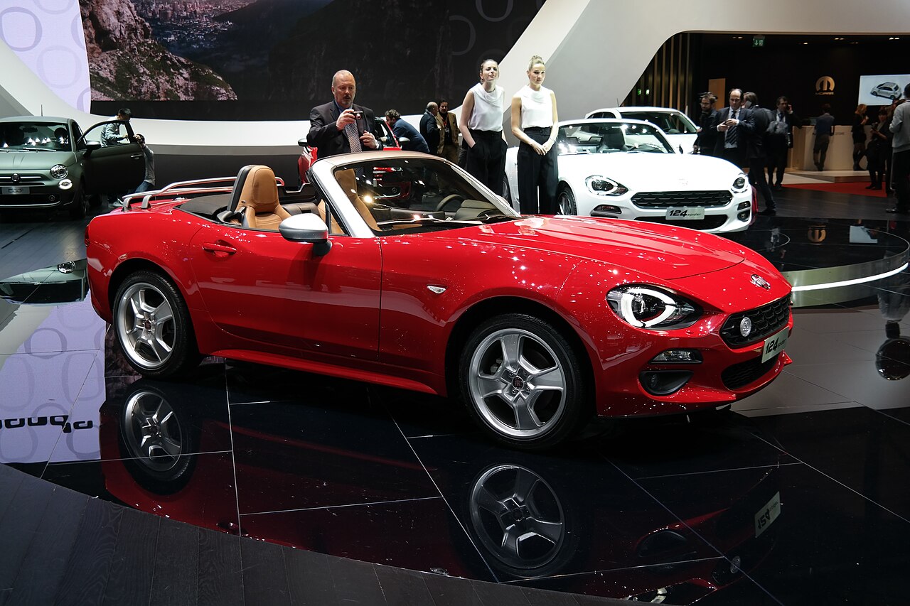 Red Fiat 124 Spider with its roof down and tan leather seats, front three-quarter view at the 2016 Geneva Motor Show.