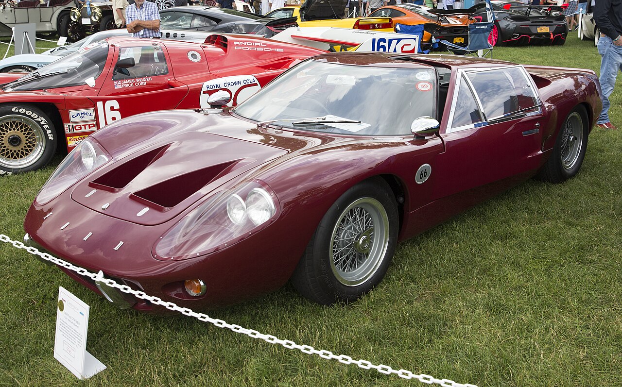 Maroon 1968 Ford GT40 Mark III with wire wheels, seen from the front left on grass at a concours.
