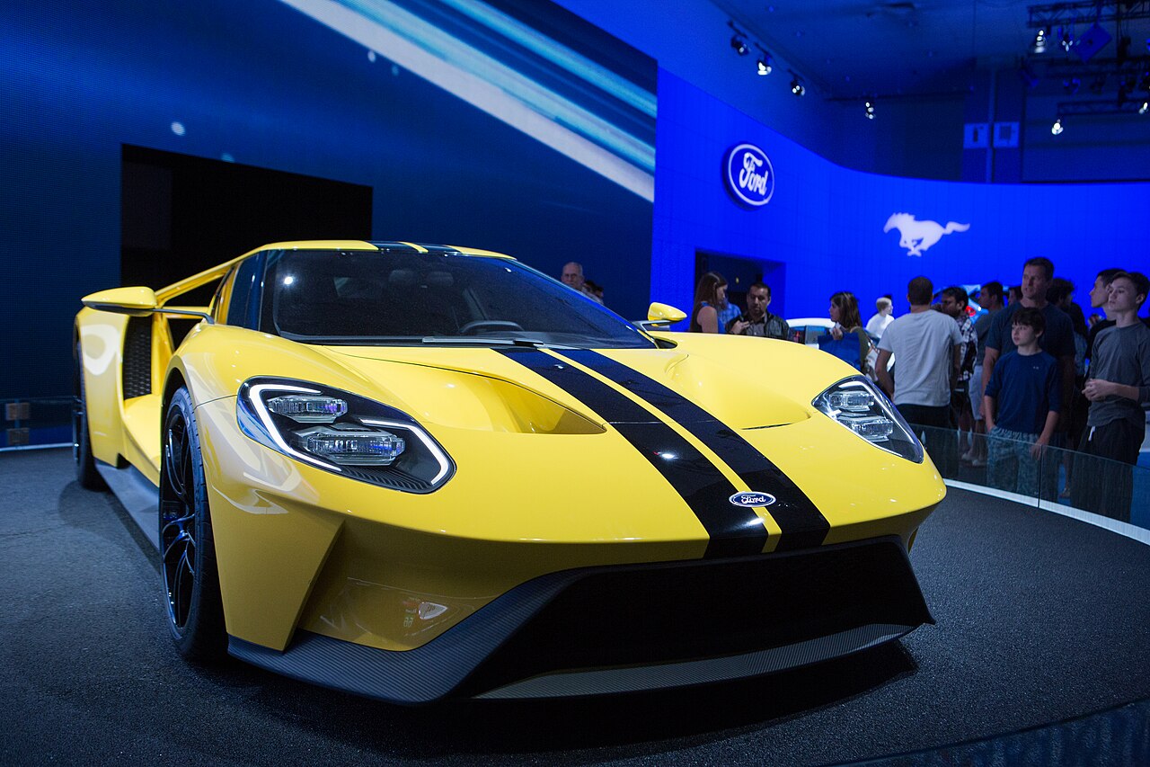 Yellow Ford GT with black stripes, front right three-quarter view on a display stage at the 2015 Los Angeles Auto Show.