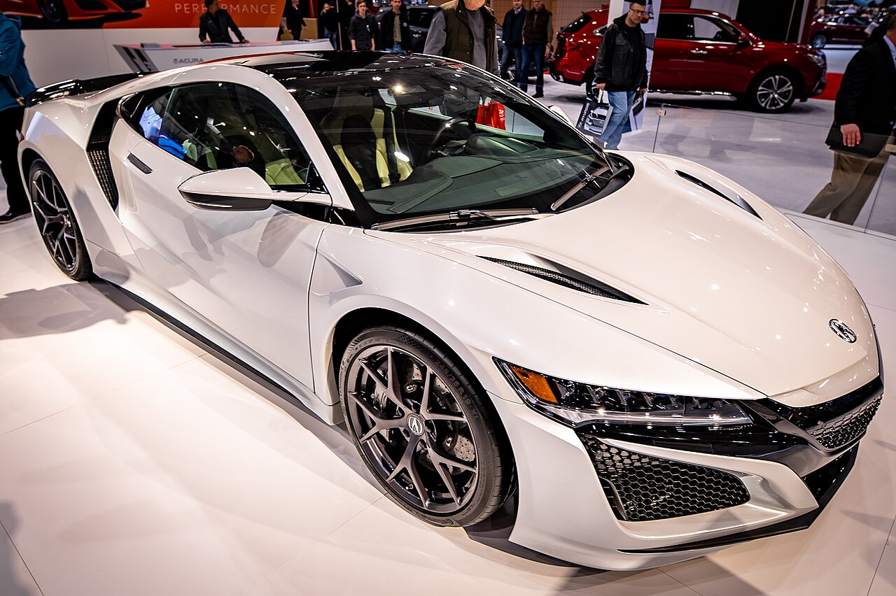 White Acura NSX in front right three-quarter view on a display floor at the Cleveland Auto Show, with visitors behind.