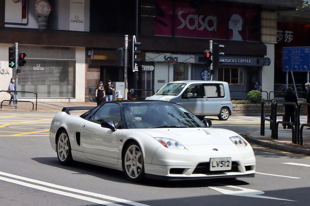 White 2002 Honda NSX with a rear wing and white wheels, front three-quarter view on a city street.