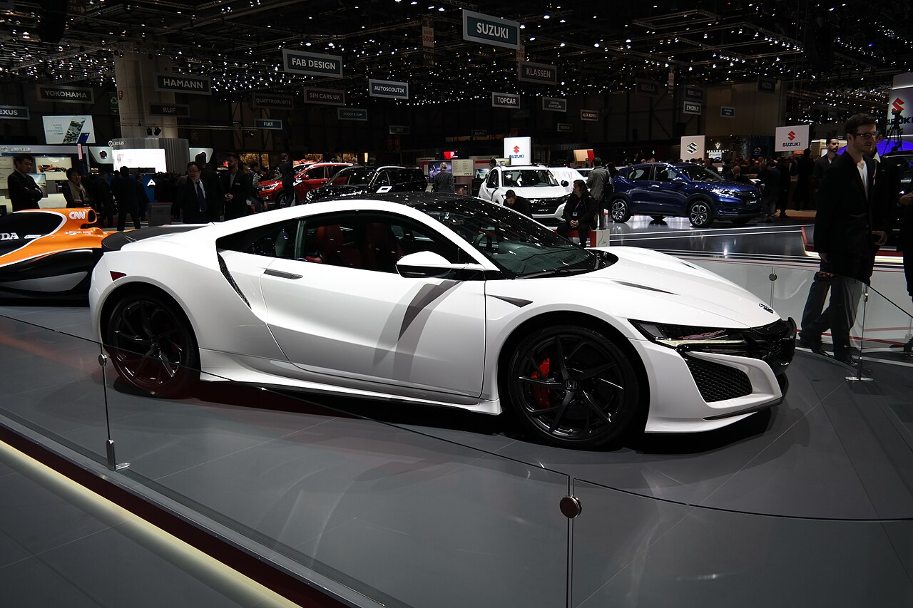 White Honda NSX with black wheels and red brake calipers, side view on a motor show stand.