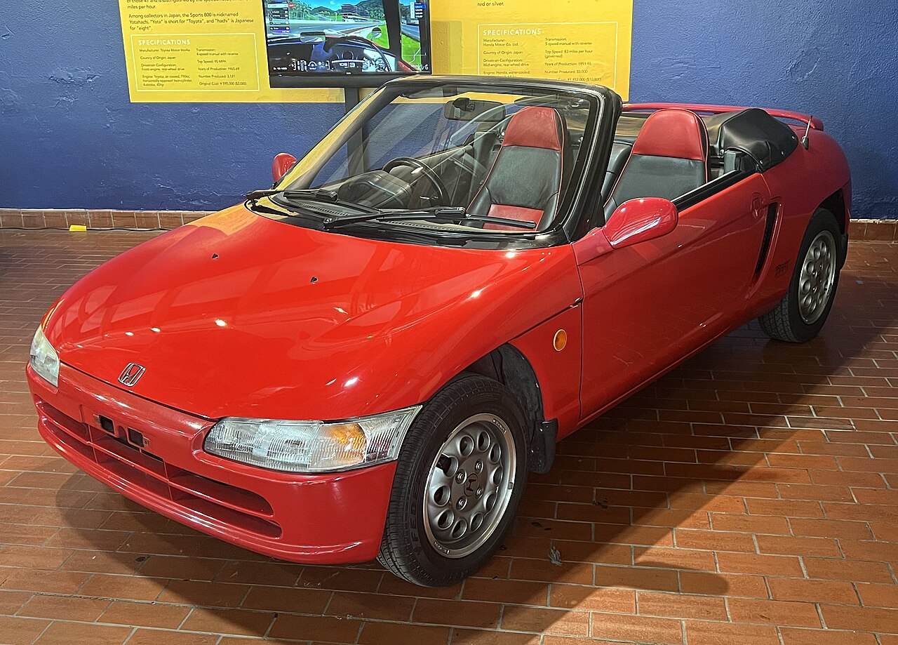 Red 1991 Honda Beat with its roof down, front three-quarter view on a brick floor in a museum.