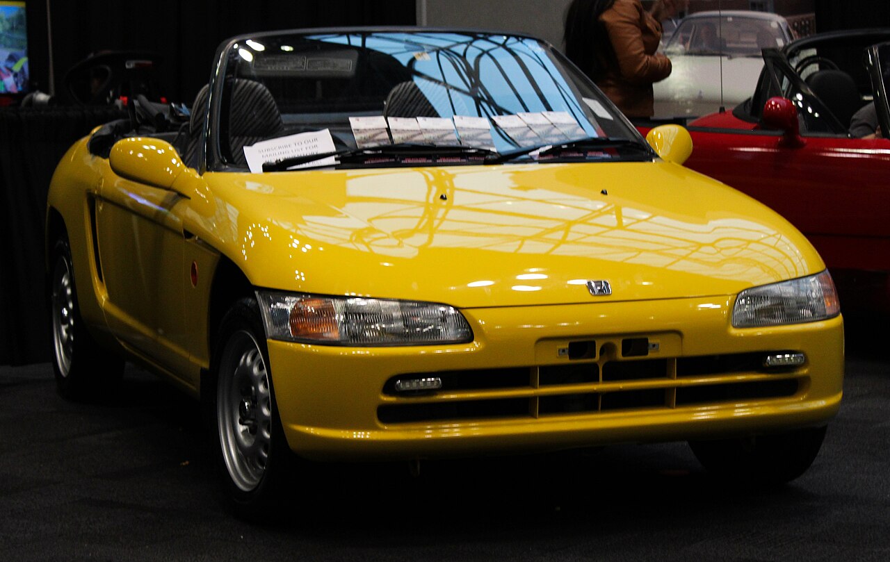 Yellow 1993 Honda Beat with its roof down, front three-quarter view at an indoor car show.