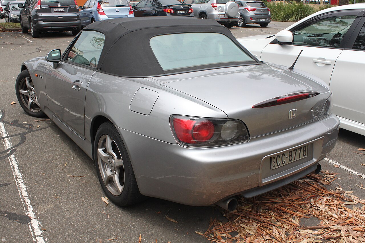 Silver 1999 Honda S2000 with its soft top up, rear left three-quarter view in a car park.