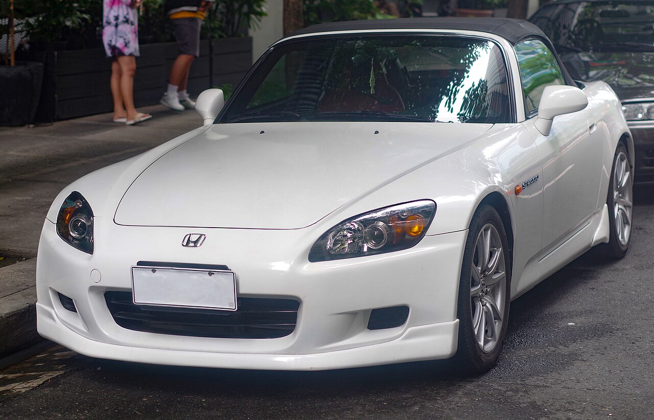 White Honda S2000 AP2 with its black soft top up, seen from the front left while parked on a city street.