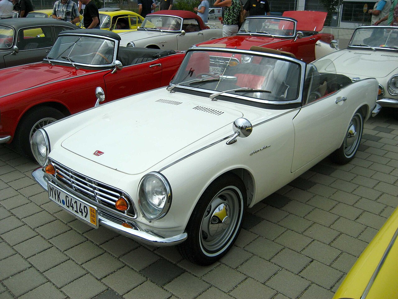 White Honda S500 roadster with its soft top folded down, front left three-quarter view at a classic car meeting.