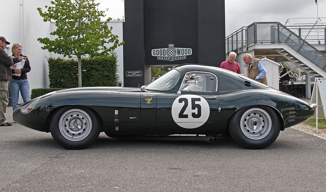 Dark green Jaguar E-type Lightweight Low Drag Coupe with a white roundel on its door, seen side-on at Goodwood.