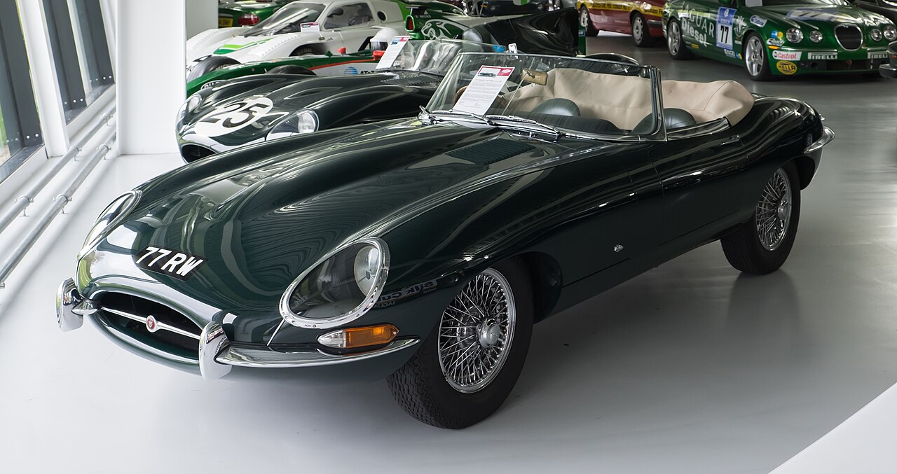 1961 Jaguar E-type Series 1 roadster in dark green with wire wheels and its hood down, front left three-quarter view in a museum.