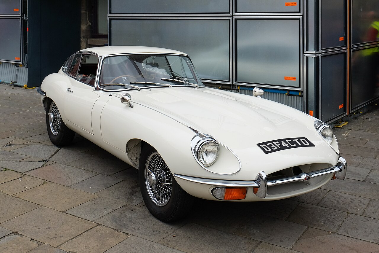 White 1968 Jaguar E-Type Series 2 coupe with wire wheels, front three-quarter view parked on paving slabs.