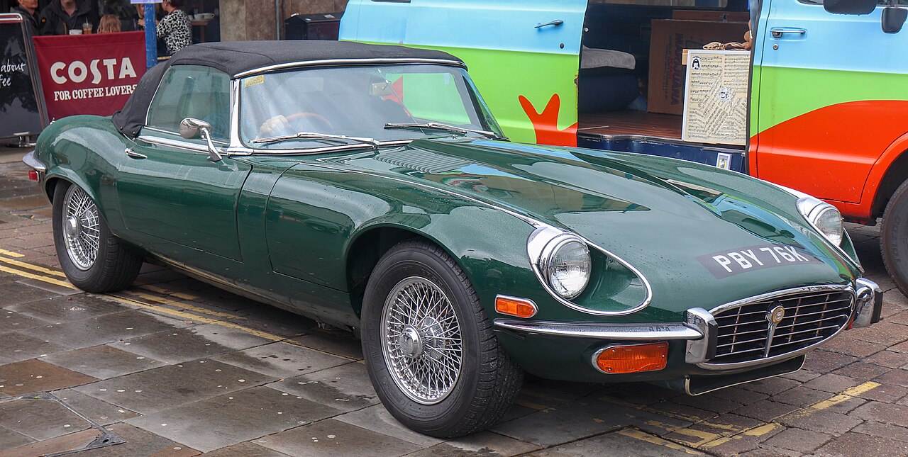 Dark green 1972 Jaguar E-Type Series 3 roadster with wire wheels and its soft top up, front right three-quarter view on a street.