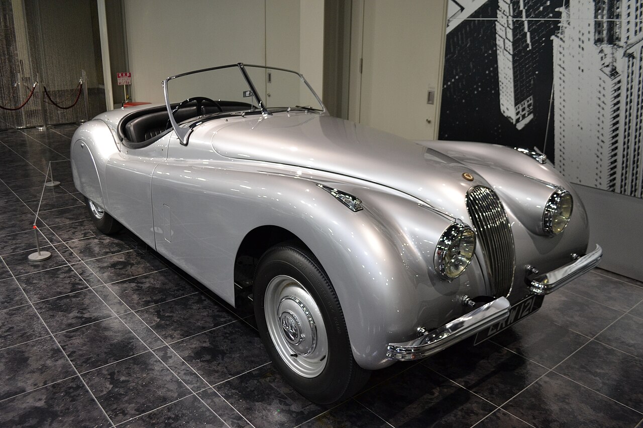 Silver Jaguar XK120 roadster with its top down, front three-quarter view in a museum.