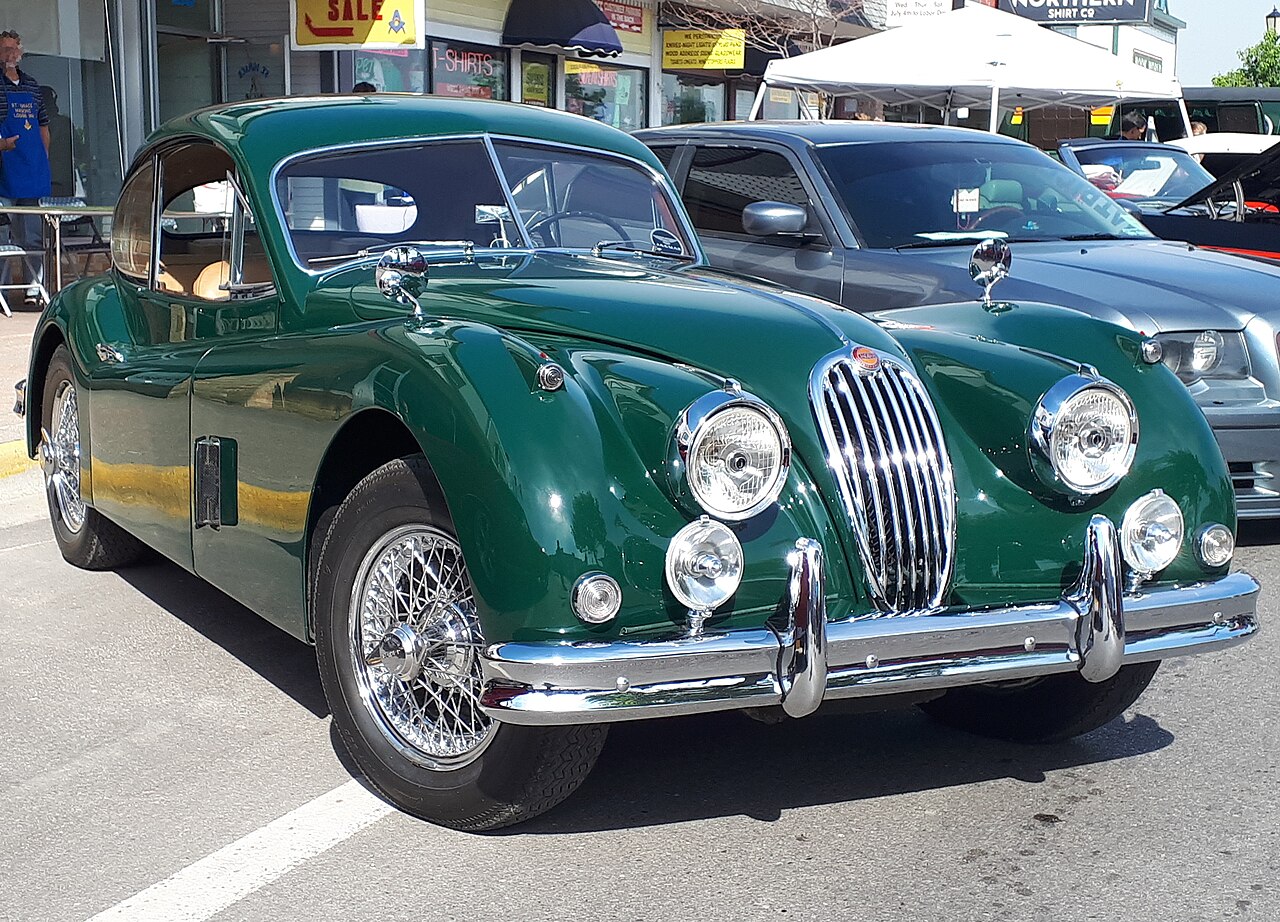 British racing green 1957 Jaguar XK140 coupe with wire wheels, front right three-quarter view at a street car show.