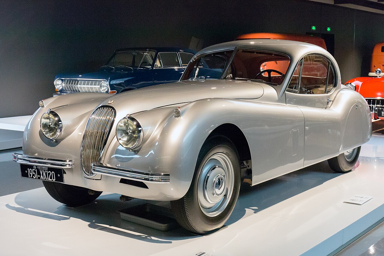 Silver 1951 Jaguar XK120 fixed-head coupe seen from the front left, on display in a museum.