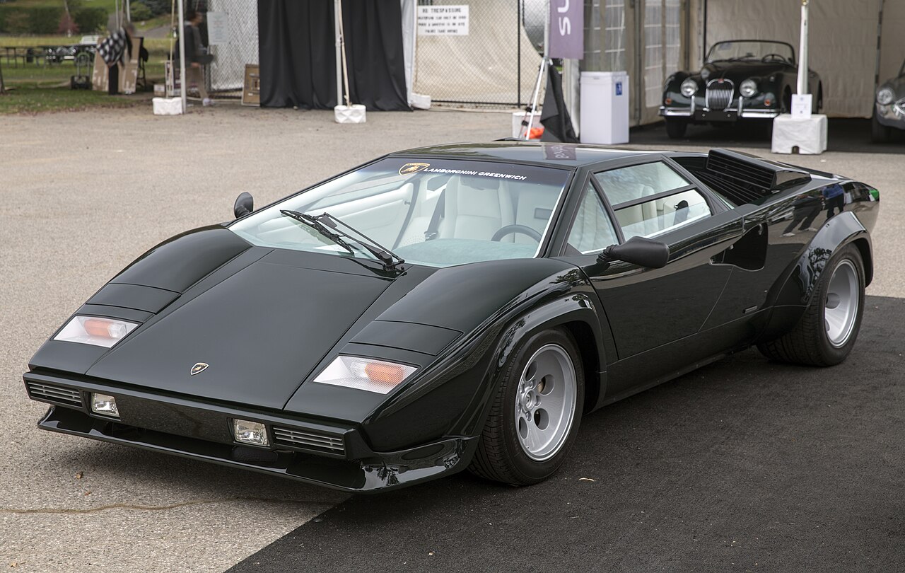 Dark green 1986 Lamborghini Countach 5000 Quattrovalvole seen from the front left, parked on tarmac at a concours.