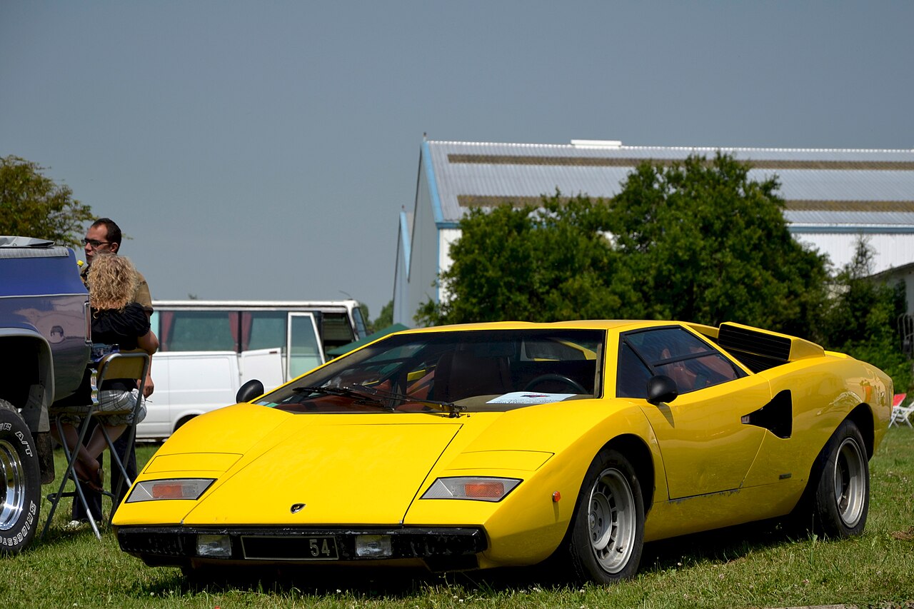Yellow Lamborghini Countach LP400, front three-quarter view parked on grass at an outdoor car show.