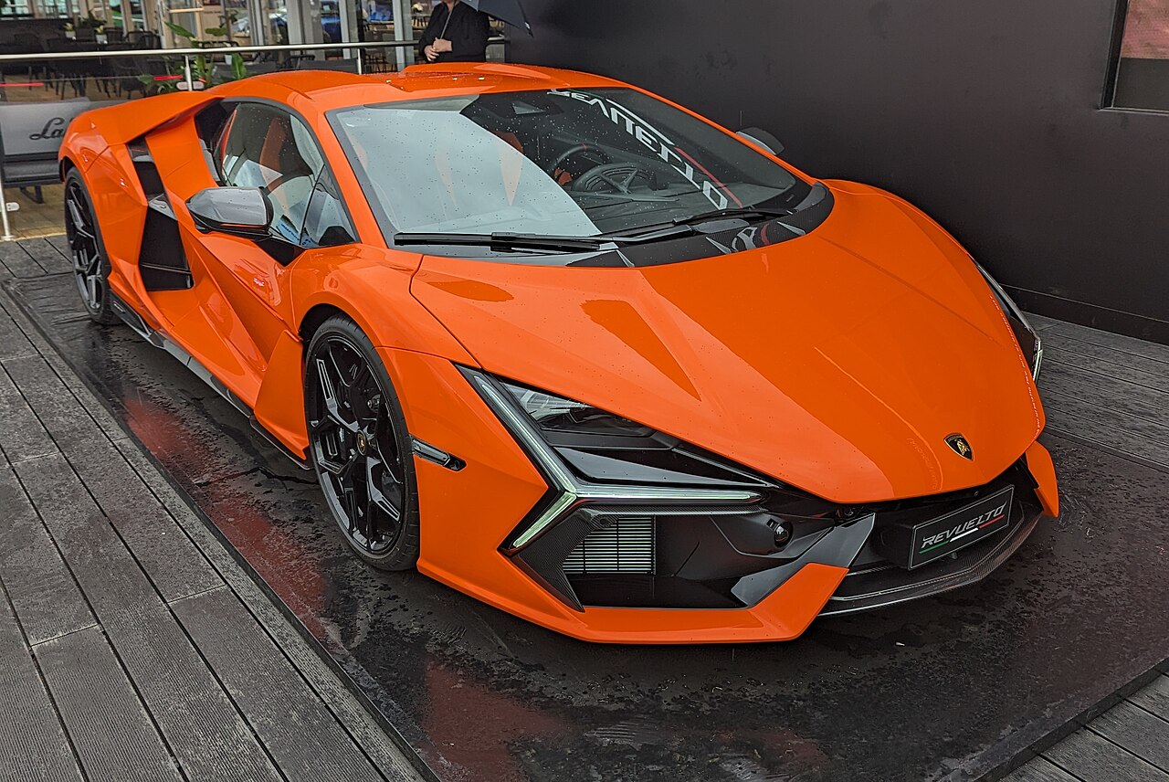 Orange 2023 Lamborghini Revuelto, front three-quarter view on a wet display platform at an outdoor event.