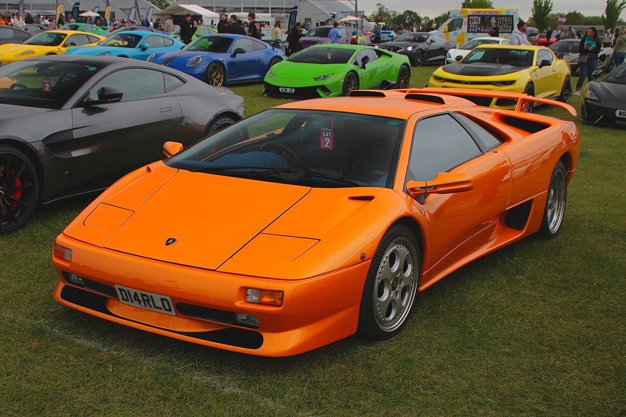 Orange 1998 Lamborghini Diablo SV, front three-quarter view on grass at a crowded car show.
