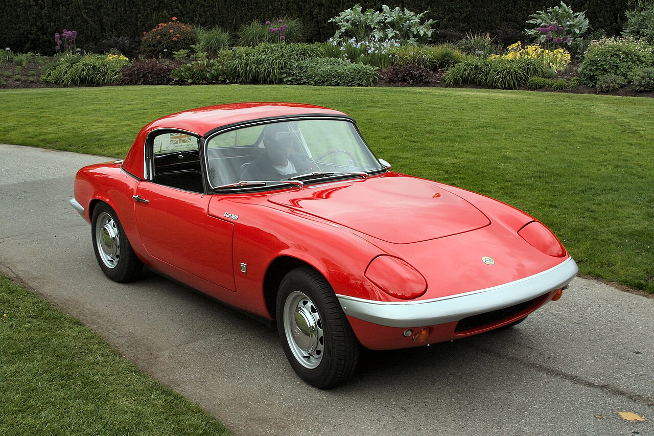 Red 1963 Lotus Elan 1600 Series 1 with its hardtop fitted, front right three-quarter view on a paved path beside a lawn.