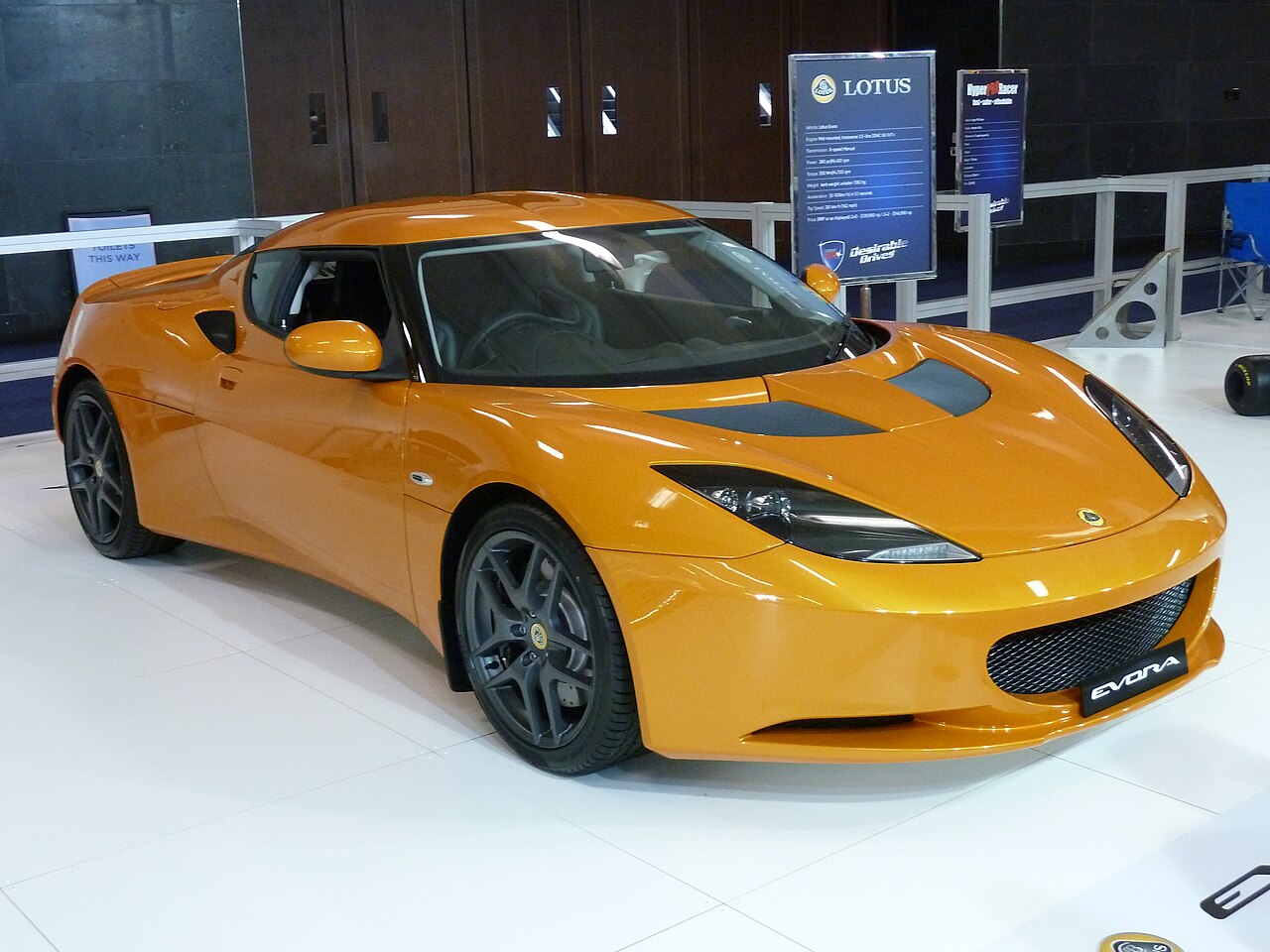 Orange Lotus Evora coupe on a white show floor, front right three-quarter view at the 2010 Australian International Motor Show.