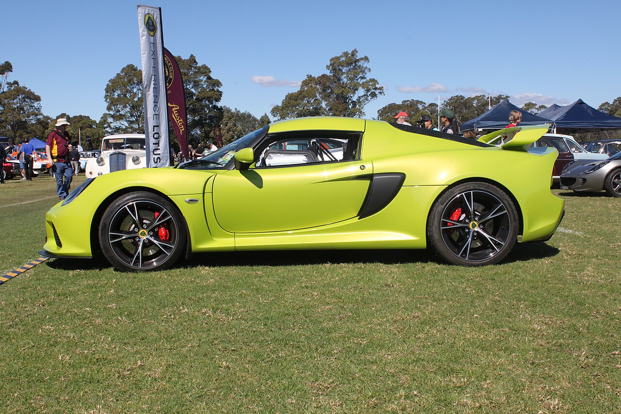 Lime green Lotus Exige S with black alloy wheels and red brake calipers, side-on on grass at a car show.
