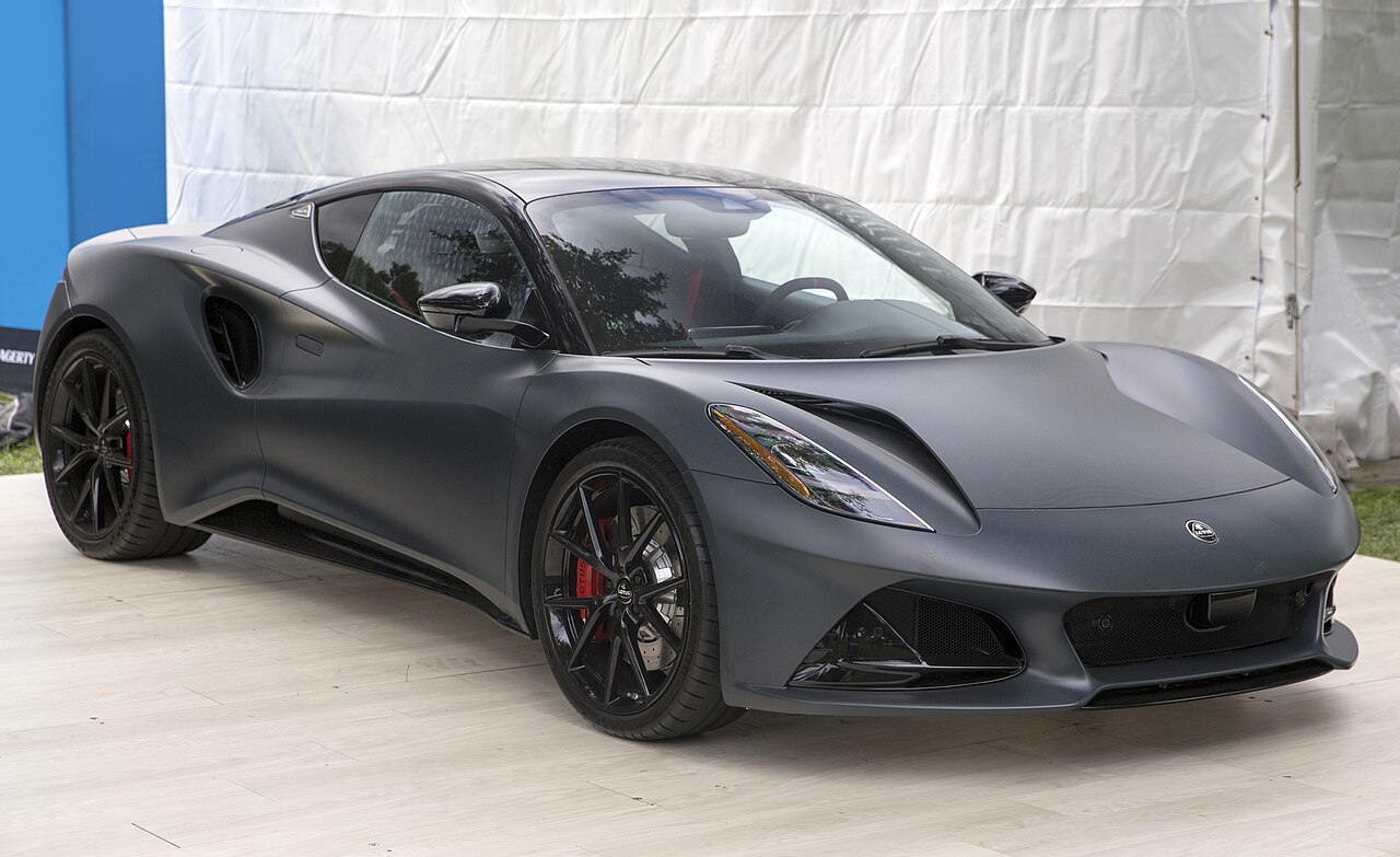 Matte black 2026 Lotus Emira V6 SE Scura, front right three-quarter view on a pale platform in front of a white tent.